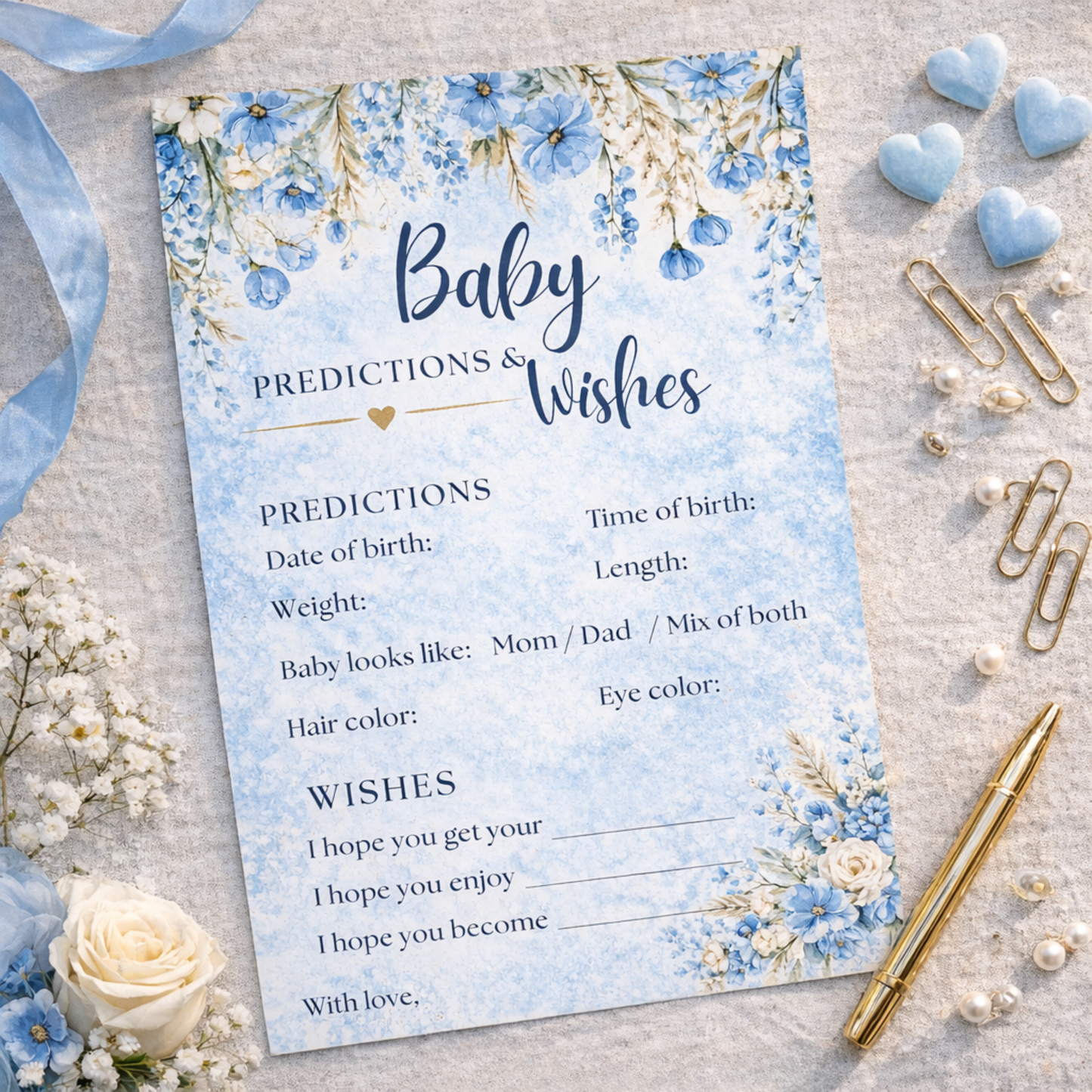 Baby shower games predictions and wishes card with floral design on a textured surface with decorative items.